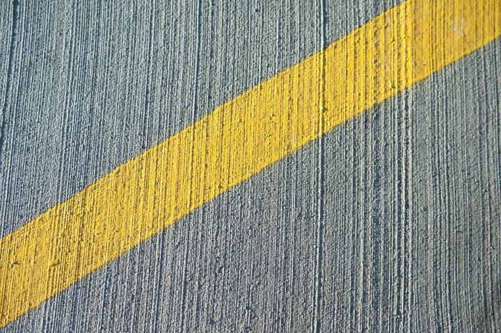 Oblique stripe of yellow paint marked on irregular gray concrete wall, close-up