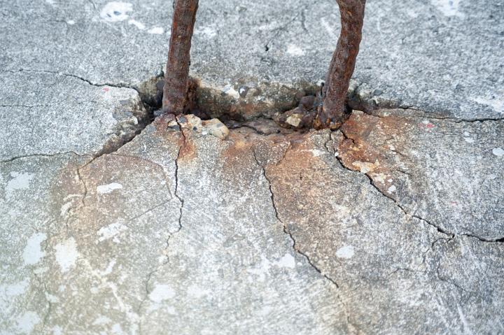 Rusted corroded metal rebar in cracked cement with oxidized rust staining the concrete