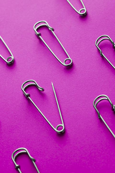 An arrangement of metal nappy safety pins, one opened and showing a sharp point, isolated on a plain purple background with copy space.