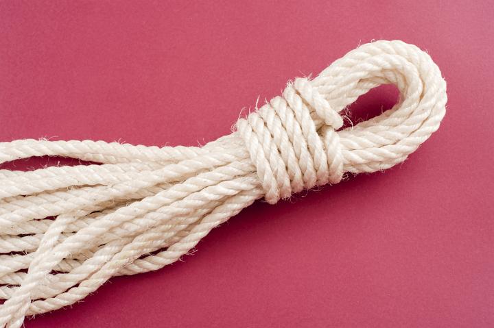 Neatly coiled and tied length of clean new white rope on a red background with copyspace