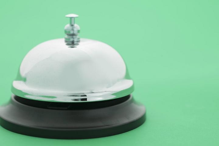 Close up of a shiny, silver service bell isolated on a plain green background.