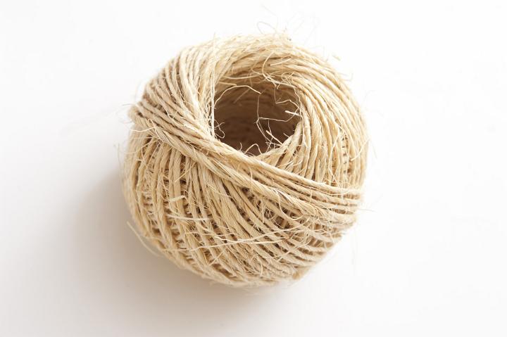 Ball of twine made from natural hemp fibers viewed high angle on white