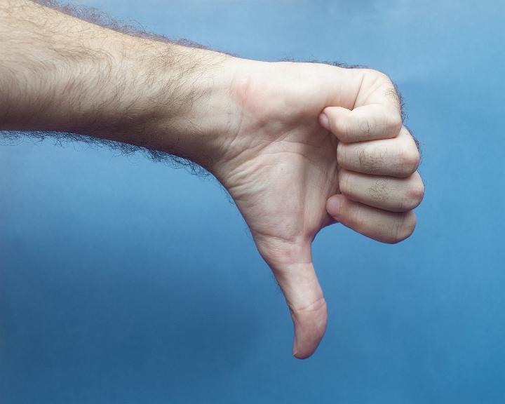 Male hand showing thumbs down, sign of dislike, disagreement or negative feedback, close-up on blue