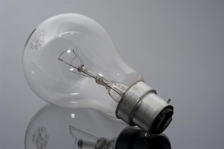 Close up Shot of Conceptual Unlit Bulb on Glossy Gray Table, Emphasizing its Reflection.