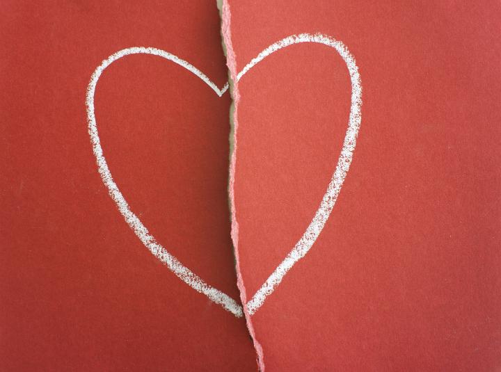 Heartbroken or broken heart concept with a hand-drawn chalk heart on a page of ripped red paper torn through the center