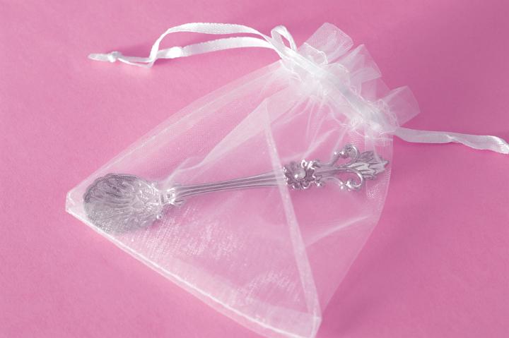 Christening Giveaway Concept - Close up Small Silver Spoon in a See Through Bag. Isolated on Pink Background.