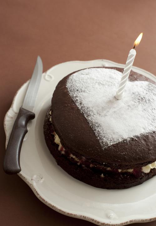 First anniversary cake with an icing sugar heart and single burning candle in a love and romance concept