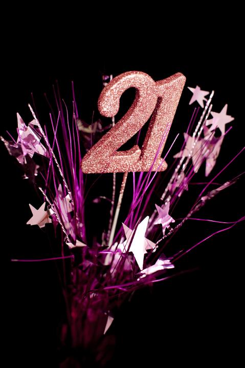 Girls 21st birthday celebrations to mark her coming of age with pink glitter numbers surrounded by a spray of stars over a dark background