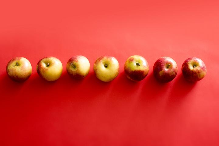 Seven apples seen from above arranged in line against red background