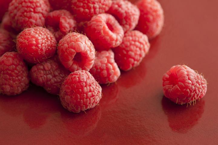 Pile of fresh raspberries with a single one to the side over a dark red background with reflections