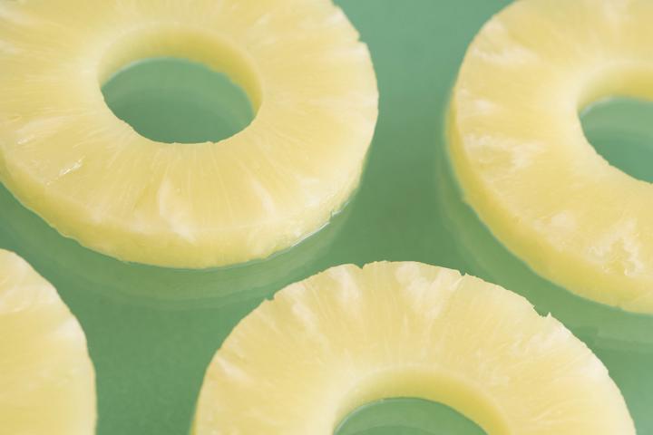 A close up of juicy, yellow sliced pineapple rings isolated on a plain green background with copy space.
