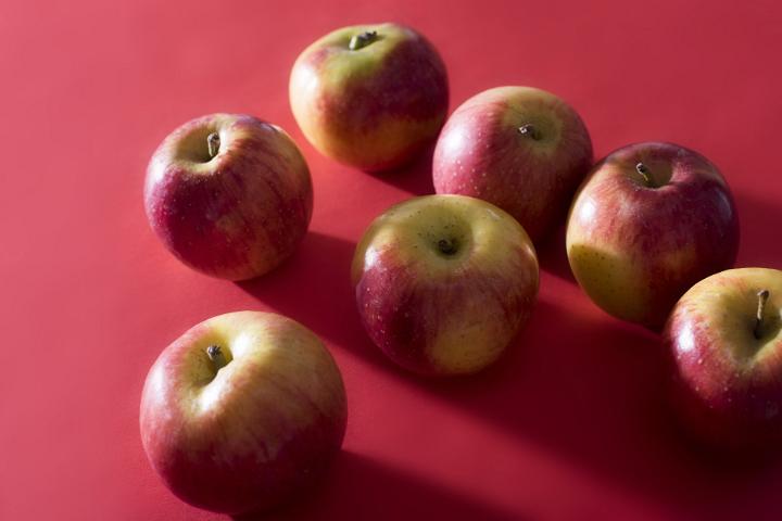 Seven apples backlit by bright light cast shadows on a plain red background.