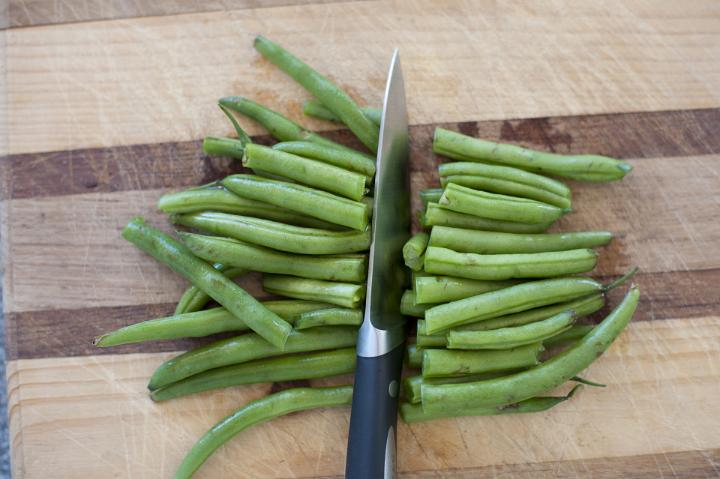 Close up Slicing Healthy Fresh Green Beans using Knife on Top of Wooden Chopping Board