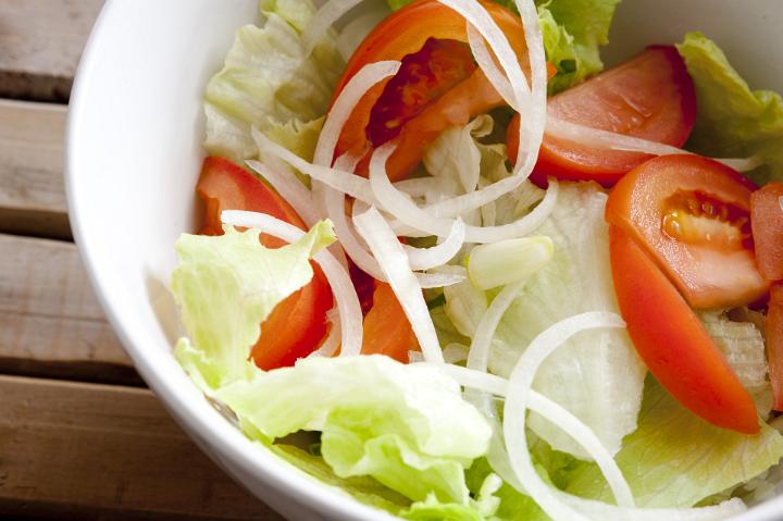 Freshly healthy mixed salad with juicy tomatoes, lettuce and onion tossed in a bowl, high angle view