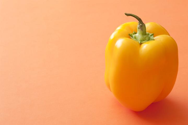 Fresh whole healthy yellow sweet bell pepper or capsicum on an orange background with copy space