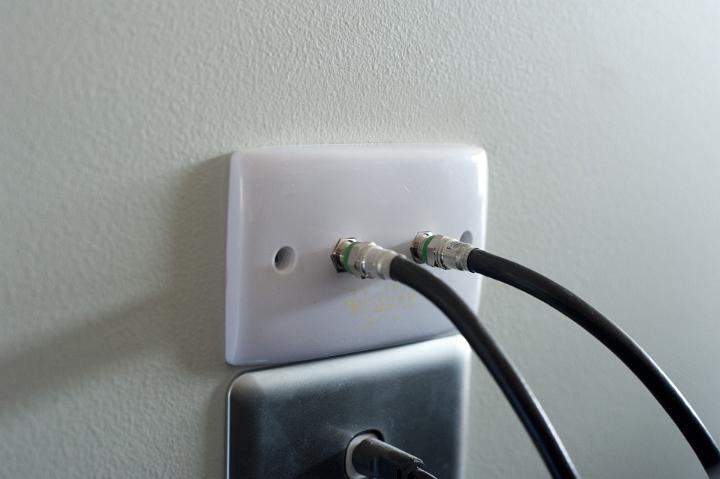 Wall socket with TV cables for comunication and broadcasting of the signal on a light grey interior wall, close up at an oblique angle