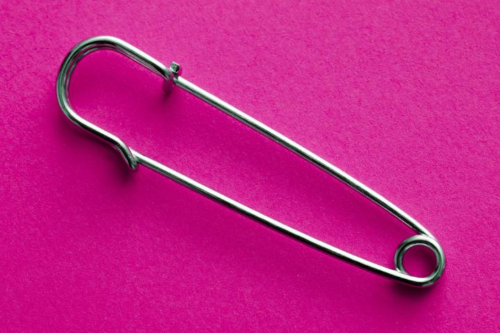 Closed safety pin on a bright pink background lying diagonally across the frame with copy space