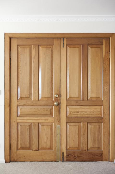 Modern closed double wooden front door with brass handle and lock in an exterior white wall of a building in a close up view