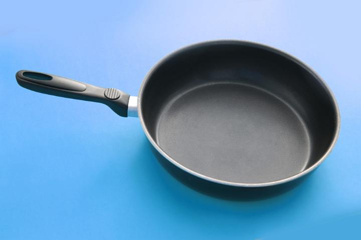 Clean empty frying pan with a non-stick coating on a turquoise blue background in a cooking and food preparation concept