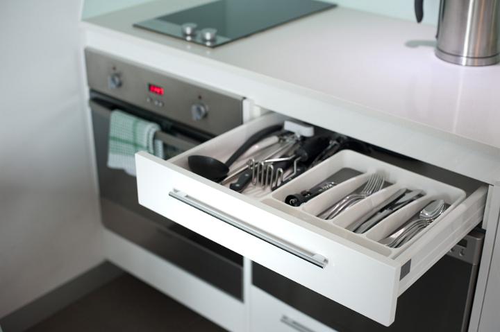 Open cutlery drawer in a kitchen cabinet with displayed kitchenware and eating utensils alongside a modern stove