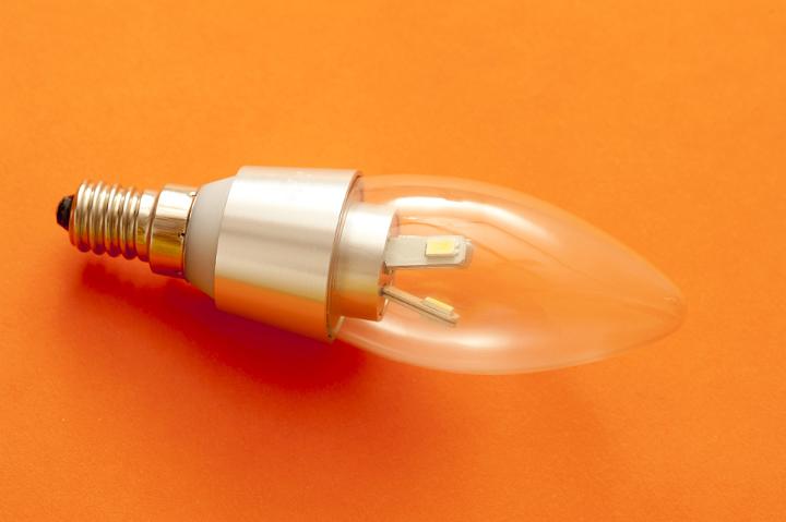 LED candle shaped light bulb with a screw fitting on an orange background showing diode detail