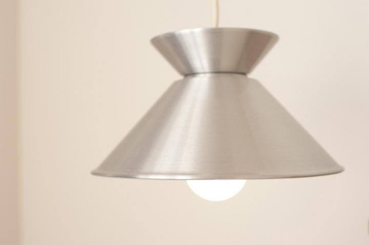 Hanging lamp with a silver metallic shade and glowing light bulb, close up view in an interior decor and power and energy concept