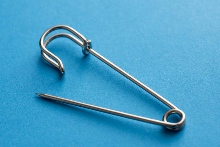 Close up of a metal kiltie safety pin isolated on a plain blue background with copy space.