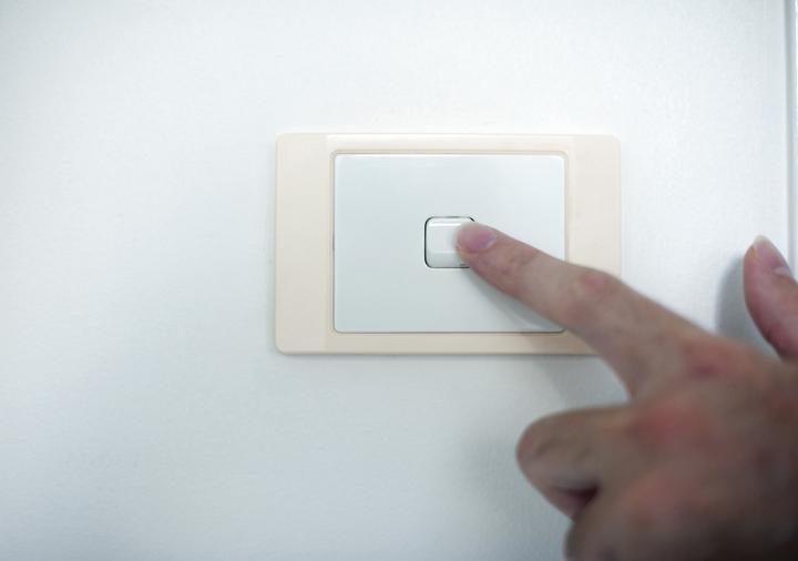 Finger switching off a wall mounted electrical light switch on a white interior house wall, close up view of the hand