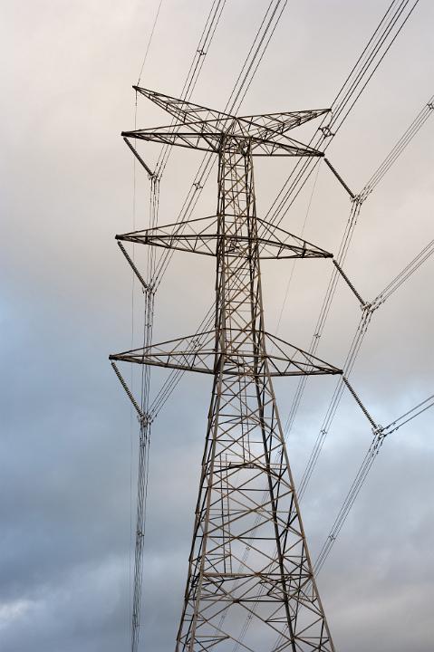 Tall steel lattice electricity pylon with high voltage cables supplying domestic and industrial power against a cloudy blue sky