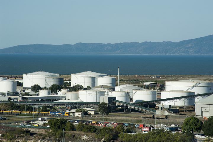 Large cylindrical storage tanks at a coastal industrial refinery for processing raw materials and resources