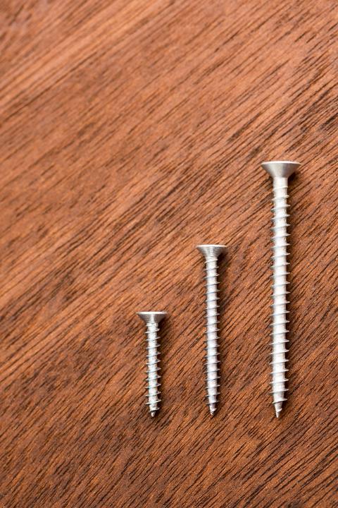 Three threaded screws in ascending sizes neatly arranged on a wood background with copy space