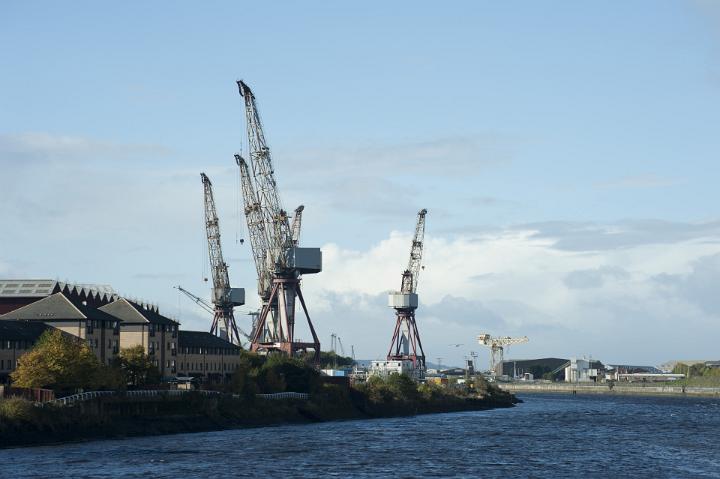 Large industrial cranes in a ship yard for boat building a loading cargo at a port against cloudy blue sky with water foreground