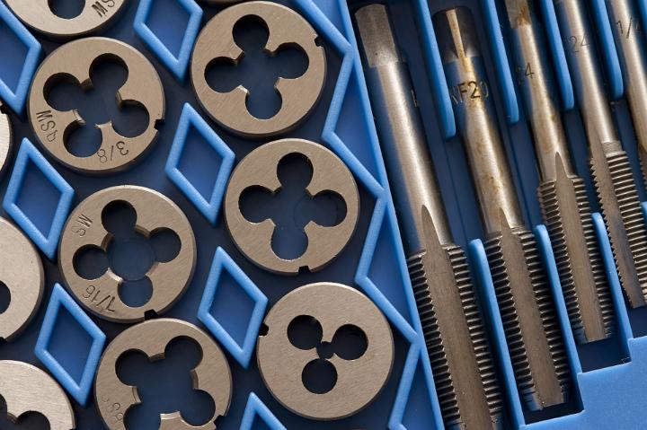 Set of taps and dies for producing screw threads, known as tapping and threading, in blue packaging, closeup view from above