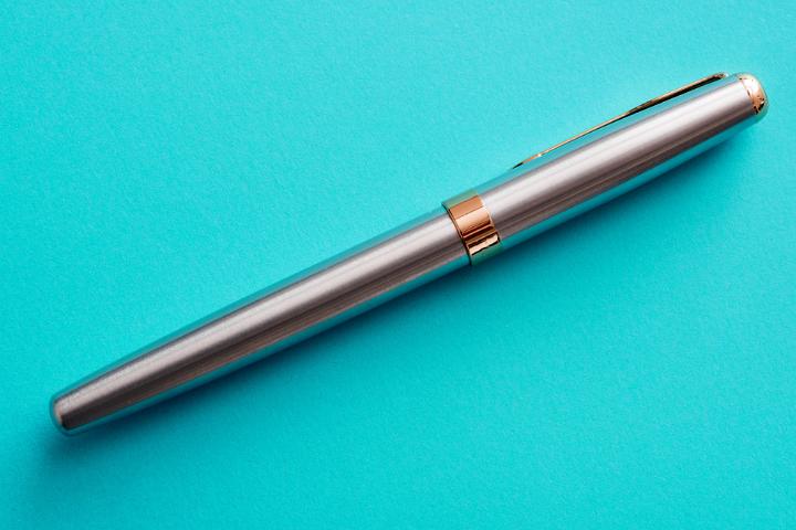 A single silver pen with cap on, isolated on a plain blue background with copy space.