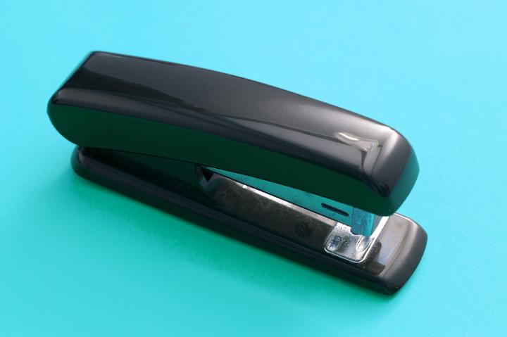 Close up Glossy Black Office Stapler Isolated on Blue Green Background
