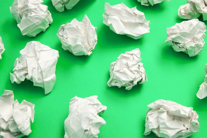 Writers block concept with balls of crumpled white paper with discarded ideas scattered on a bright green background in a full frame view
