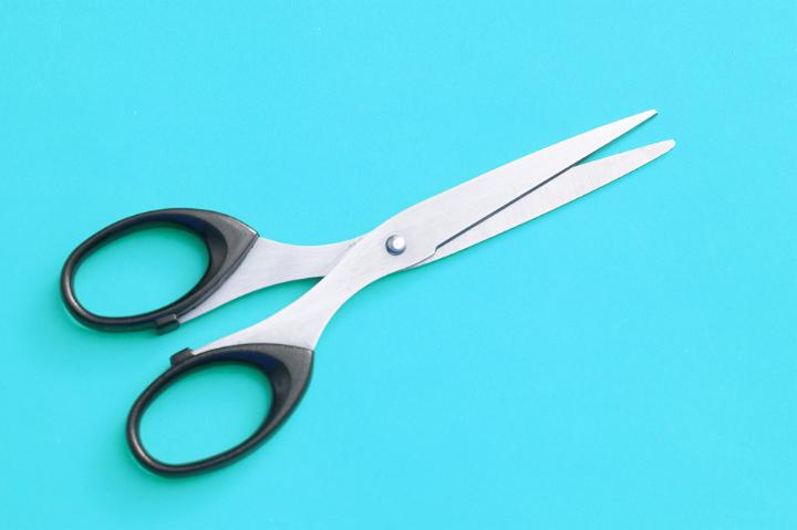 Close up Brand New Pair of Office Scissors Isolated on Cyan Background