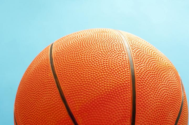 Close up texture of an orange basketball showing the stippling on the surface over a turquoise blue background