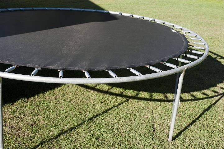 Small trampoline with a metal frame standing outdoors in the sunshine on a green lawn, close up view