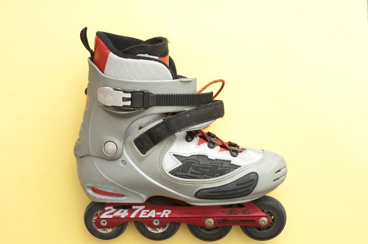 Modern inline roller skate or roller blade with four wheels aligned in a row on a yellow background with copyspace