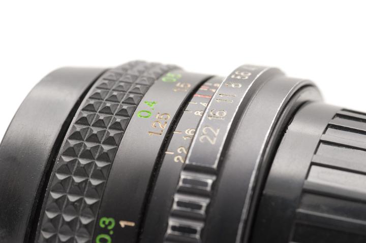 Close Up of Manual SLR Camera Lens with Aperture and Focal Length Setting Numbers in front of White Background