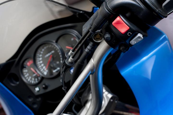 Close Up of Motorcycle Kill Switch and Ignition Switch on Handlebars of Blue Bike with Dashboard Gauges in Background