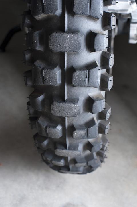 New tyre detail on a motorbike showing the rubber tread parked on a grey surface