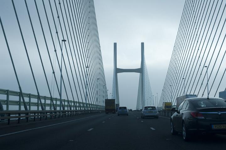 A busy motorway cable stay bridge with passing cars and traffic on a stormy overcast day.