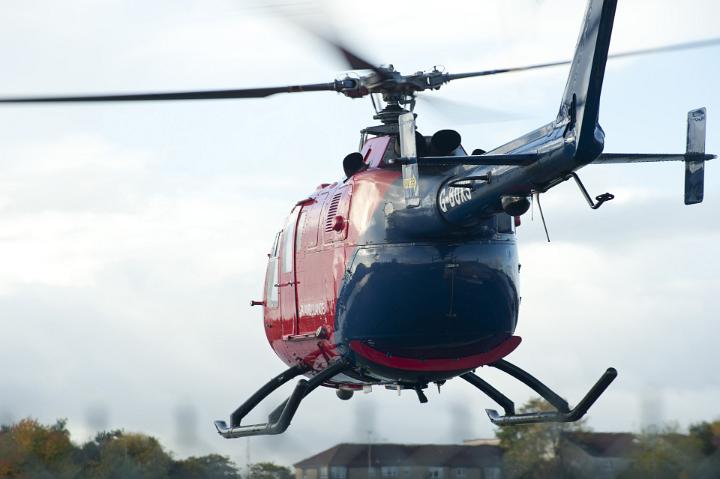 Red Helicopter Hovering with Blurred Rotating Blades as seen from Behind