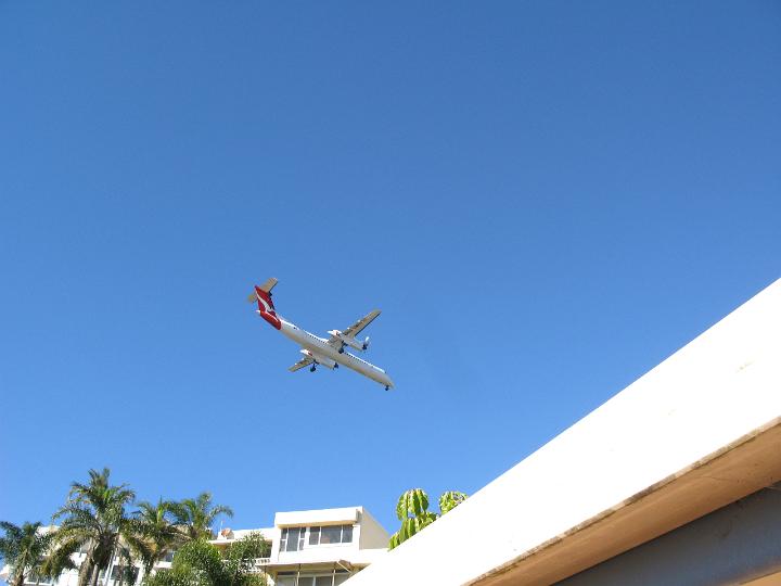 Aircraft coming on to land over the tops of whitewashed houses in a tropical resort conceptual of travel and summer vacations