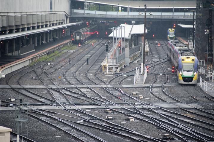 Empty railway tracks cross and intersect as three trains sit stationary at a city railway stations.