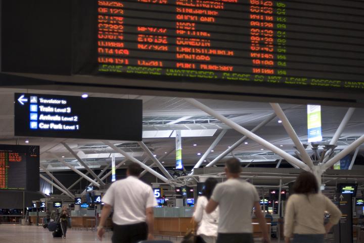 Passengers in an airport terminal building below the departures or arrivals board detailing the flights
