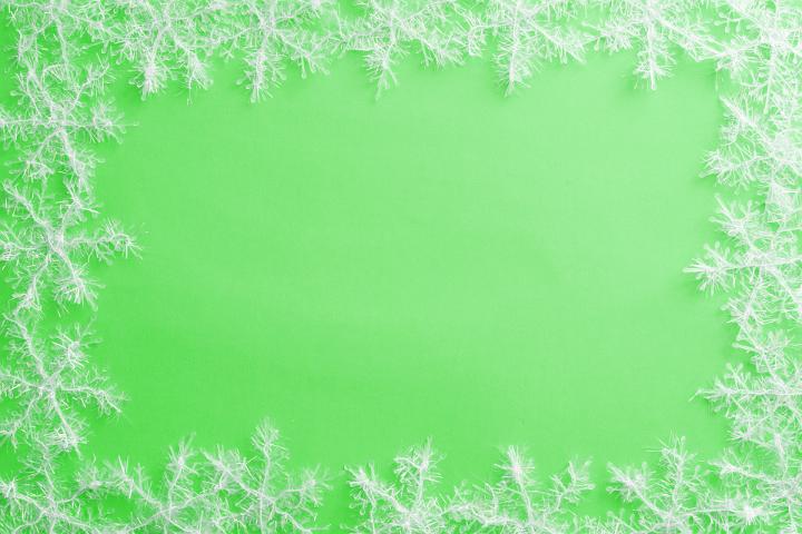 Border of dainty white Christmas snowflake decorations on a green background with copy space for a seasonal greeting