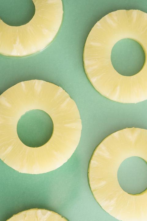 High angle view of pineapple cut in slices arranged on green background